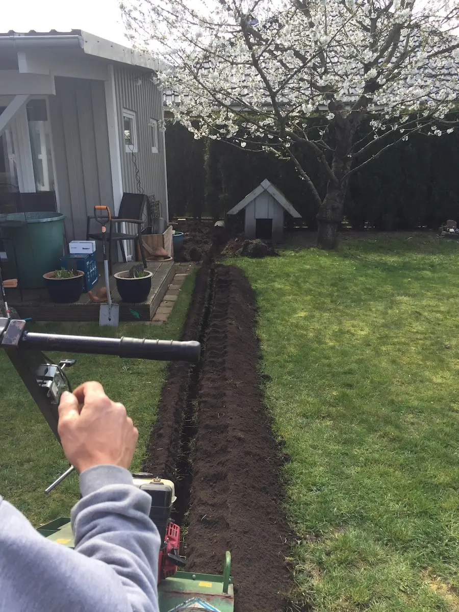 Offener Leitungsgraben im Rasen vor einem Gartenhaus