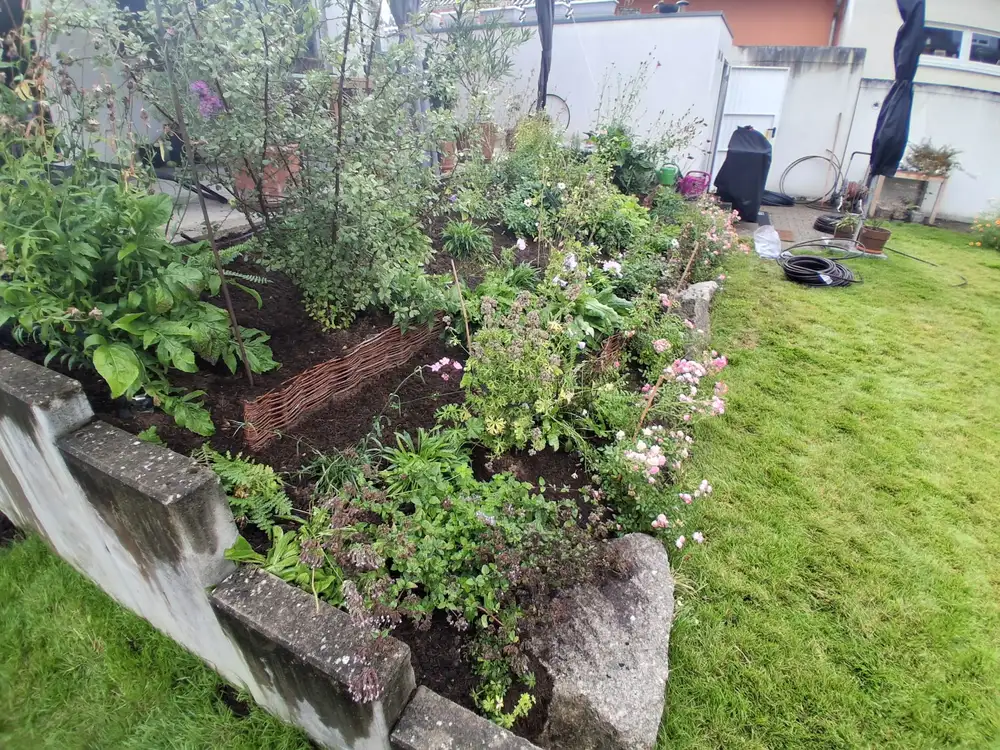 Blühendes Staudenbeet an einer Natursteinmauer im Garten