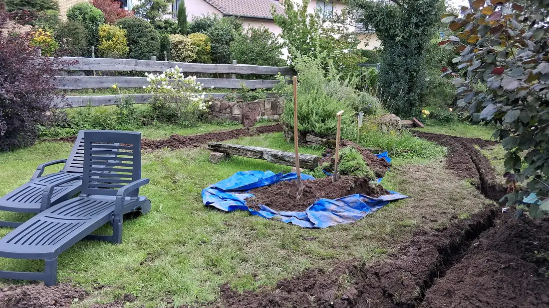 Garten mit Liegestuhl, jungem Baum und offenen Leitungsgräben