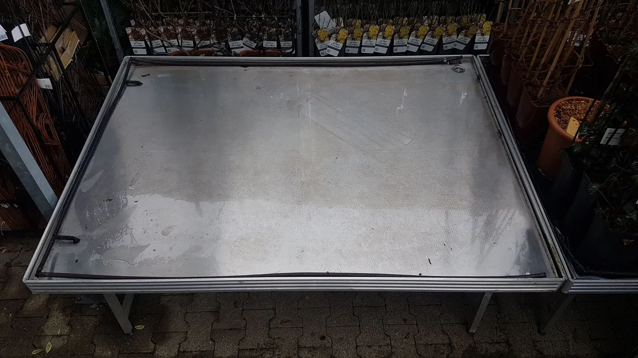 Leerer Pflanztisch mit Aluminiumwanne im Außenbereich eines Gartencenters